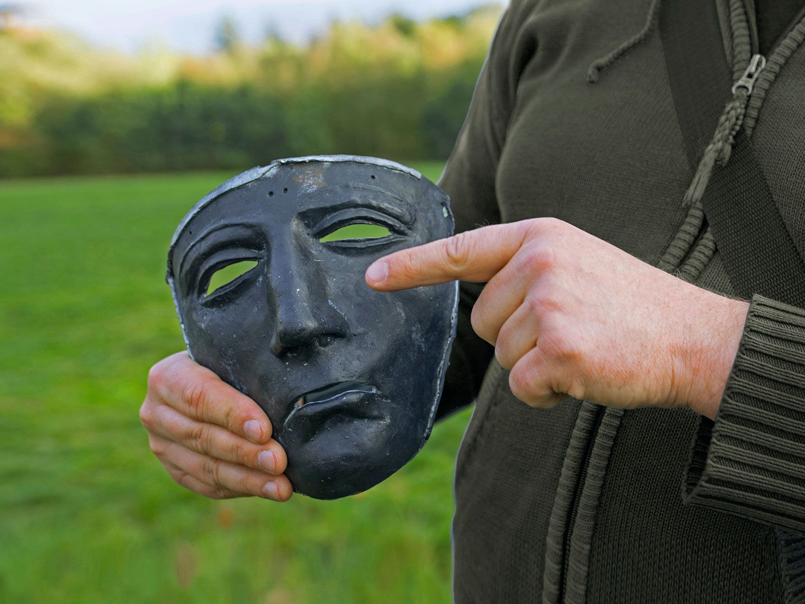 Mann zeigt auf Nachbildung der Reitermaske in seiner Hand.