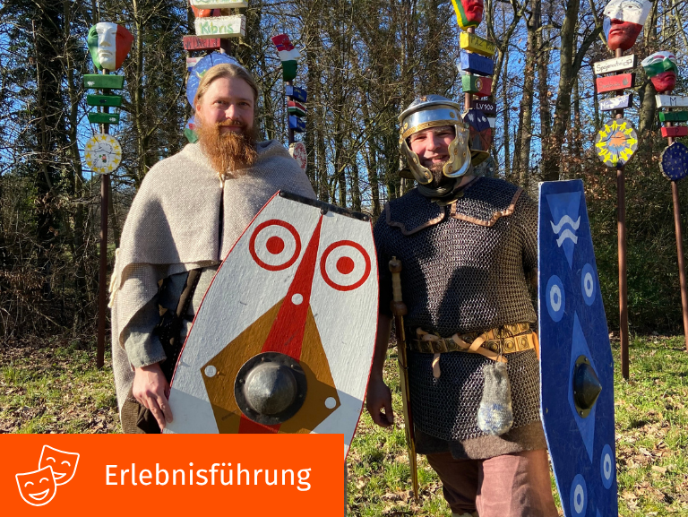 Zwei lächelnde Männer, die mit Schilden und Rüstungen ausgestattet sind. 