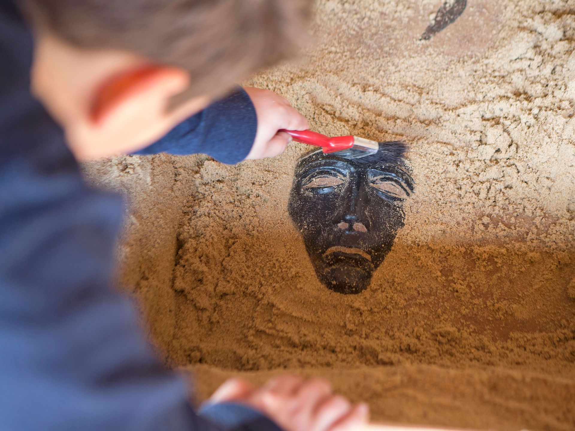 Kind legt im Sand ein Abbild der Reitermaske frei.