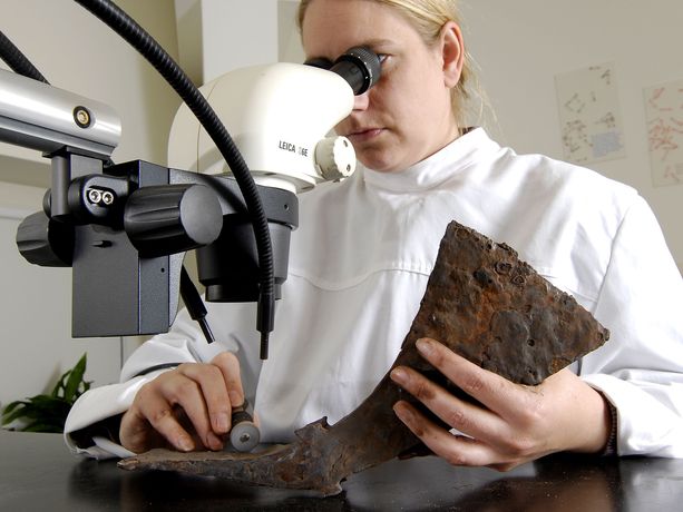 Ein Fundstück wird von einer Wissenschaftlerin unter dem Mikroskop untersucht.